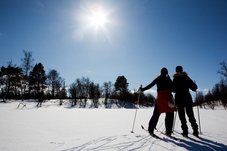 Två personer på skidor som står och tittar mot solen en vacker och snöfylld dag