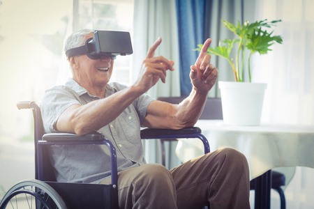 Happy senior man on wheelchair using VR headset at home