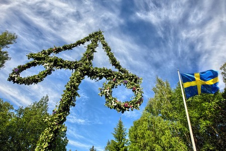 Midsommarstång och svensk flagga mot en blå himmel med slöjmoln